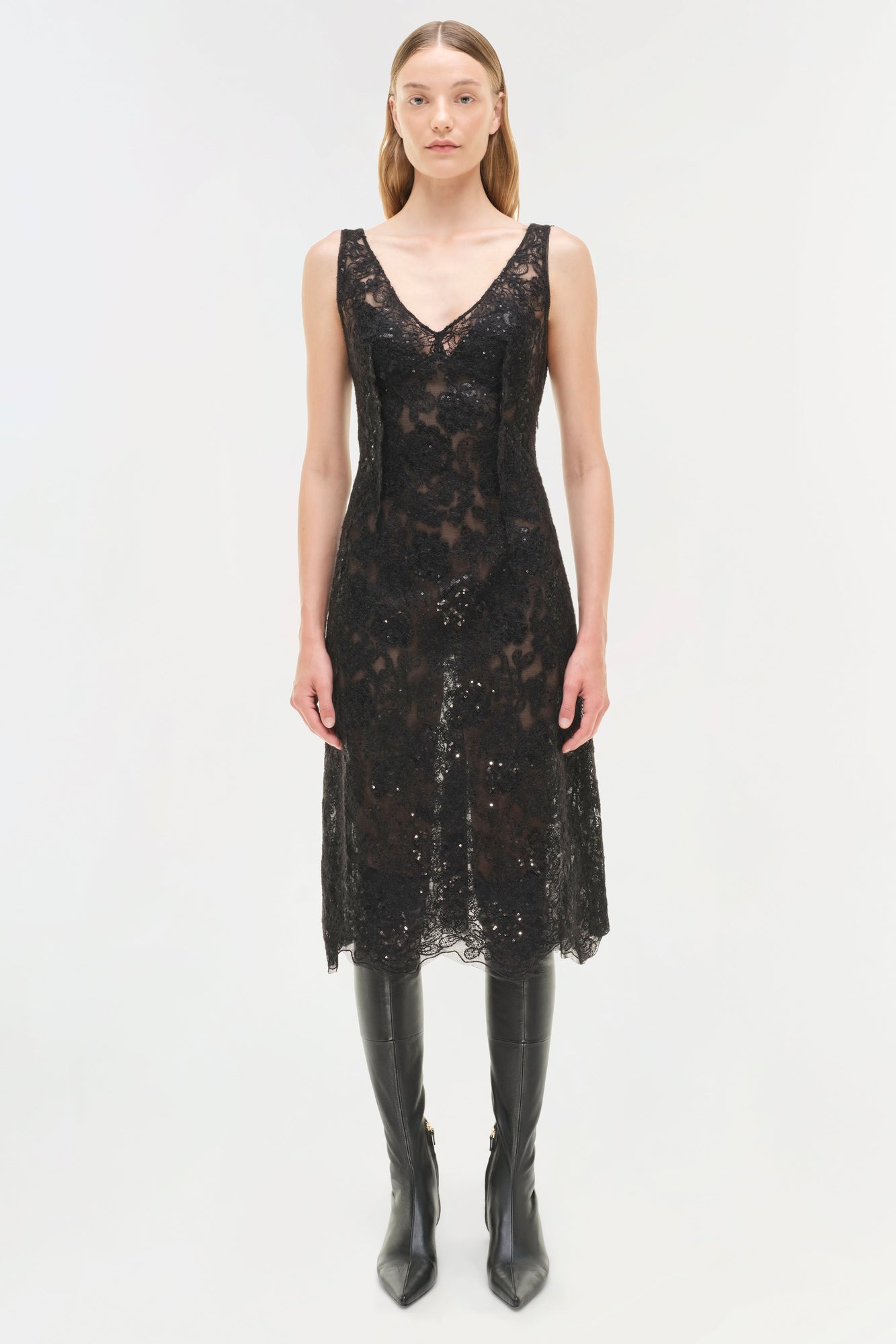 Black sequin lace sleeveless midi dress with V-neckline worn with black knee-high boots.