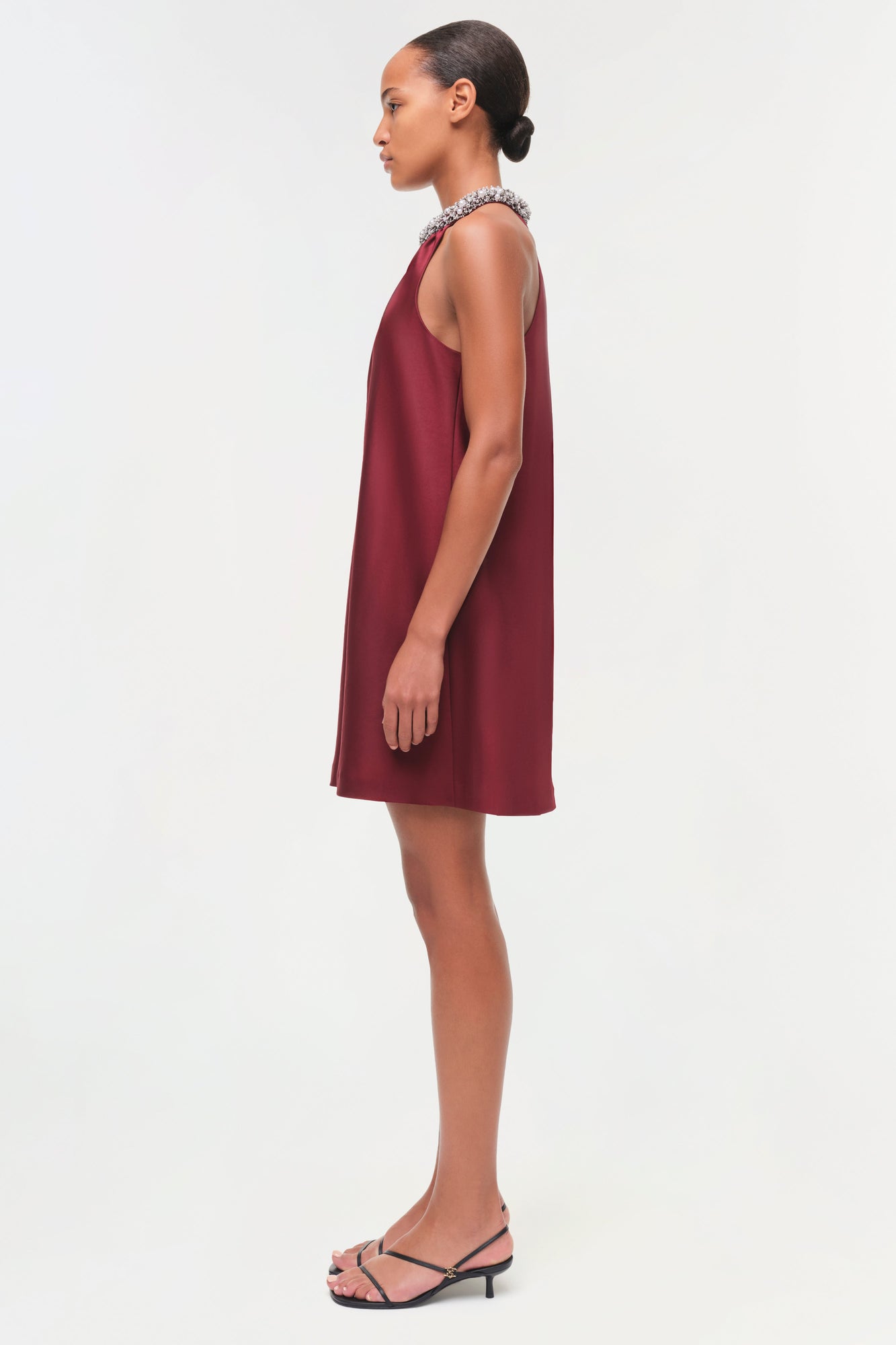 Burgundy satin sleeveless shift dress with embellished neckline, shown on model in profile view.