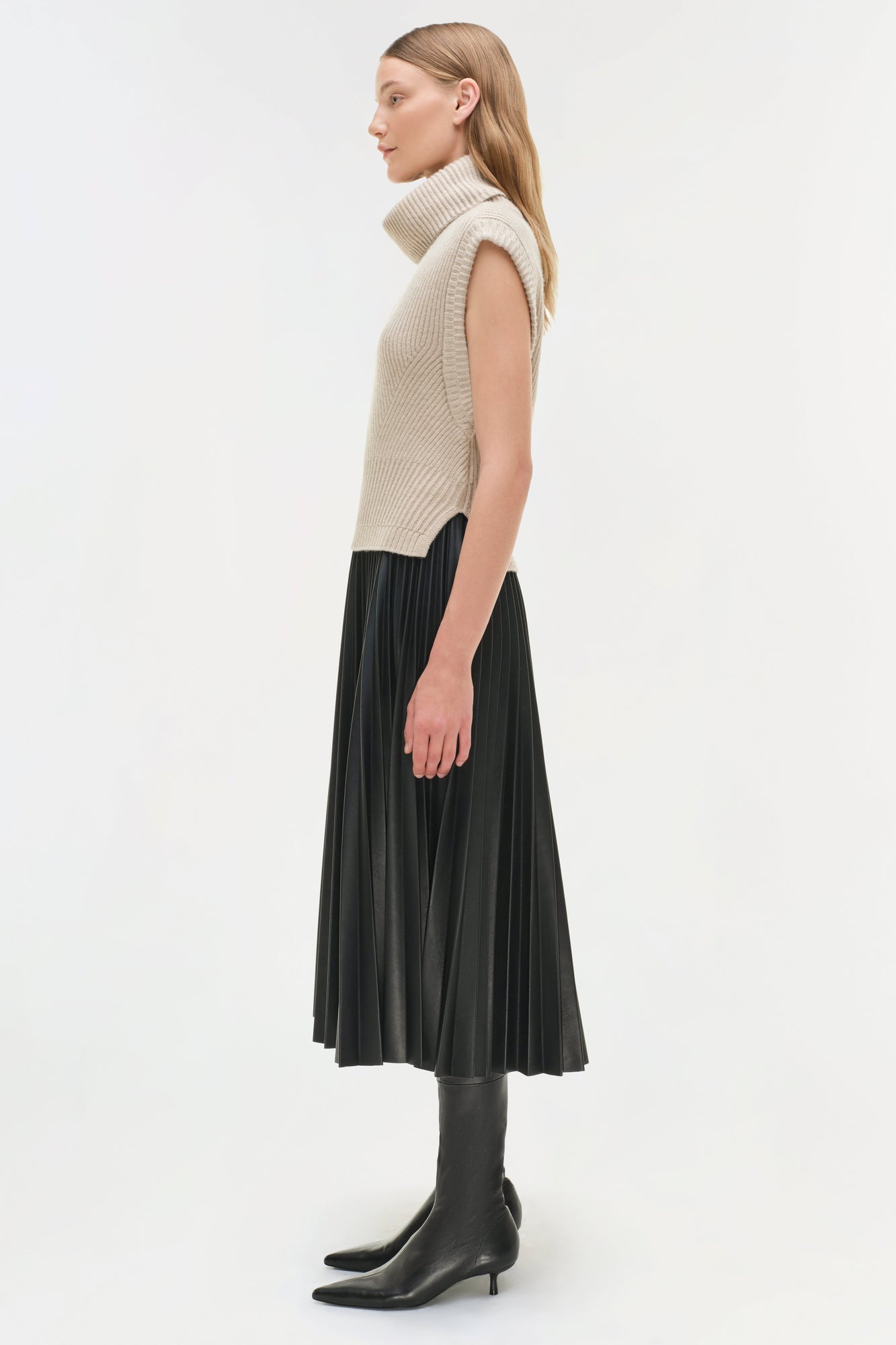 Black pleated midi skirt with high waist, paired with cream sleeveless turtleneck sweater and black ankle boots.