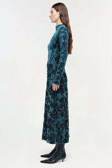 Teal velvet midi dress with black floral print, long sleeves, and ruched side detail, worn with black boots.