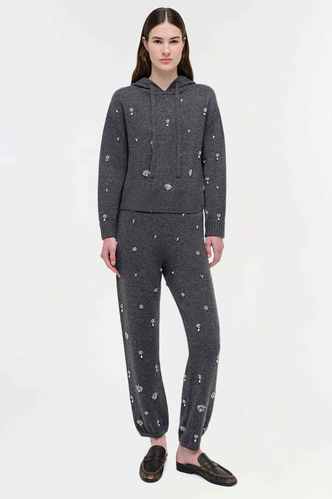 Woman wearing charcoal gray cashmere hoodie and joggers with scattered silver crystal embellishments throughout.