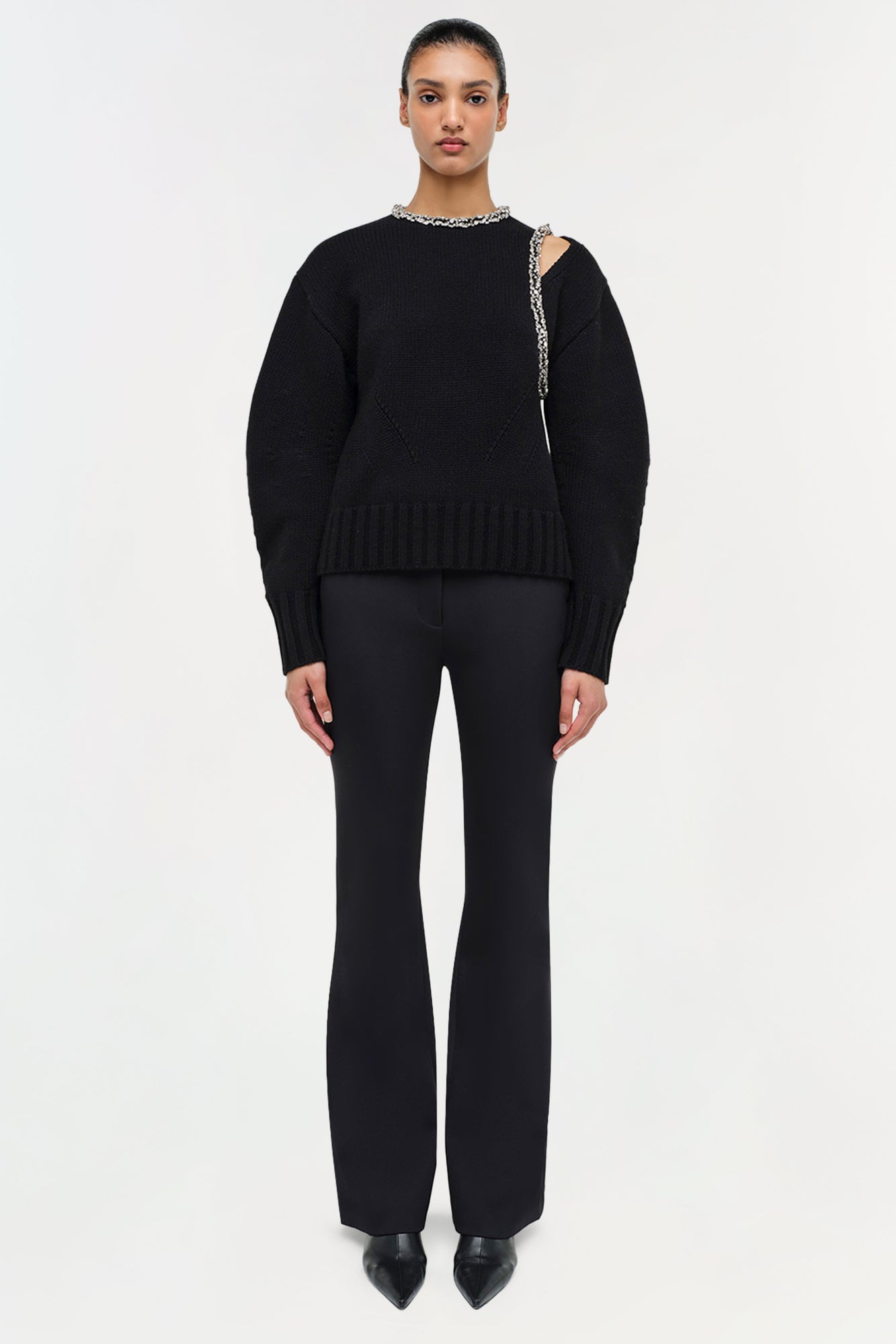 Black pullover with embellished neckline and shoulder cutout detail, styled with matching black flared pants.
