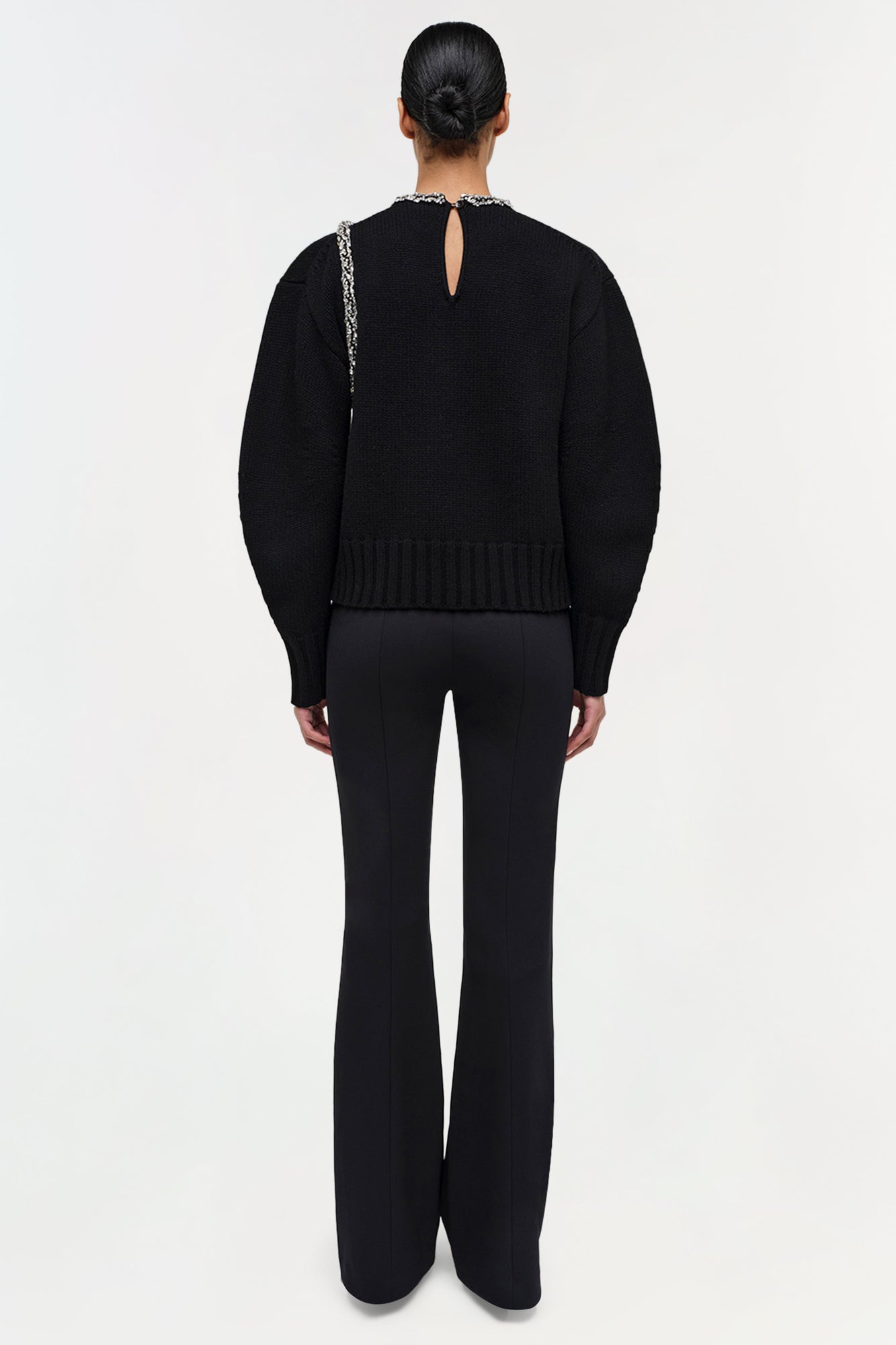 Black pullover with embellished neckline and keyhole back cutout, paired with black flared pants.