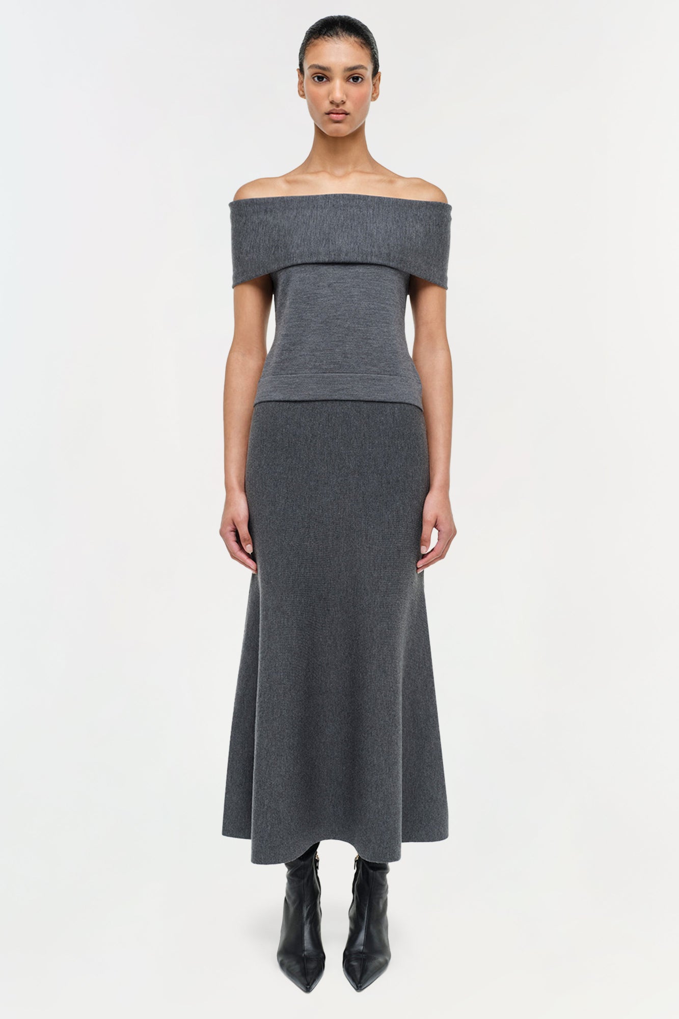 Woman wearing charcoal gray wool skirt with off-shoulder top and black boots against white background.