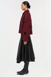 Black leather midi skirt with A-line silhouette, styled with burgundy cardigan and black boots.