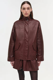 Burgundy leather jacket with high neckline, front snap closure, and patch pockets worn over matching skirt.