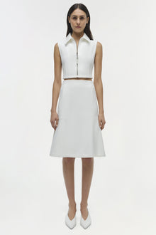 White sleeveless crop top with collared neckline and front zipper, paired with matching midi skirt.