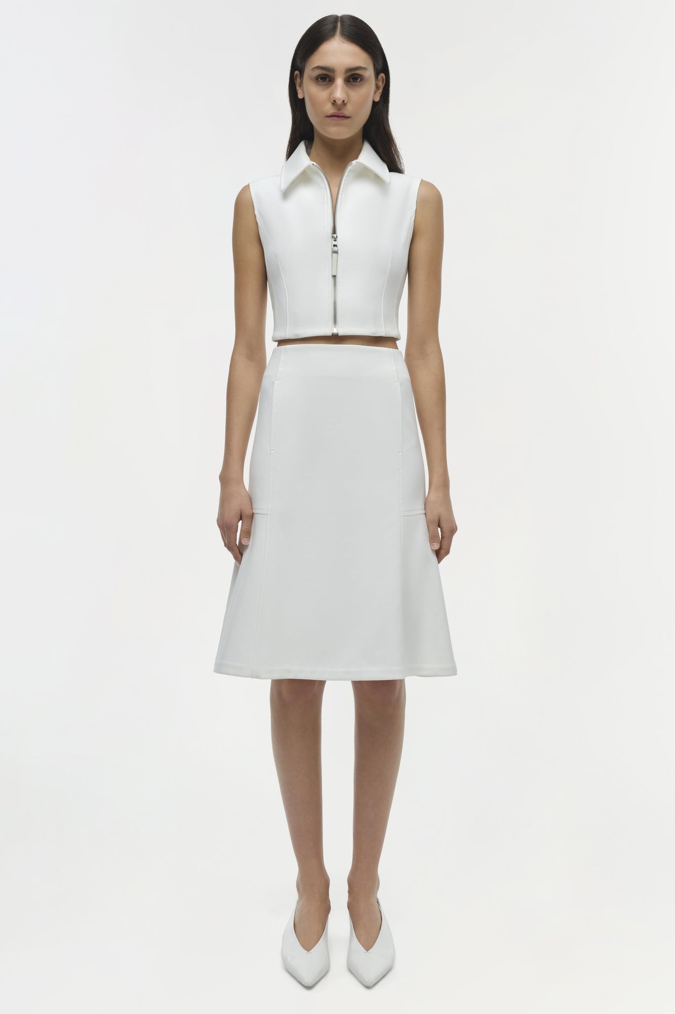White sleeveless crop top with collared neckline and front zipper, paired with matching midi skirt.