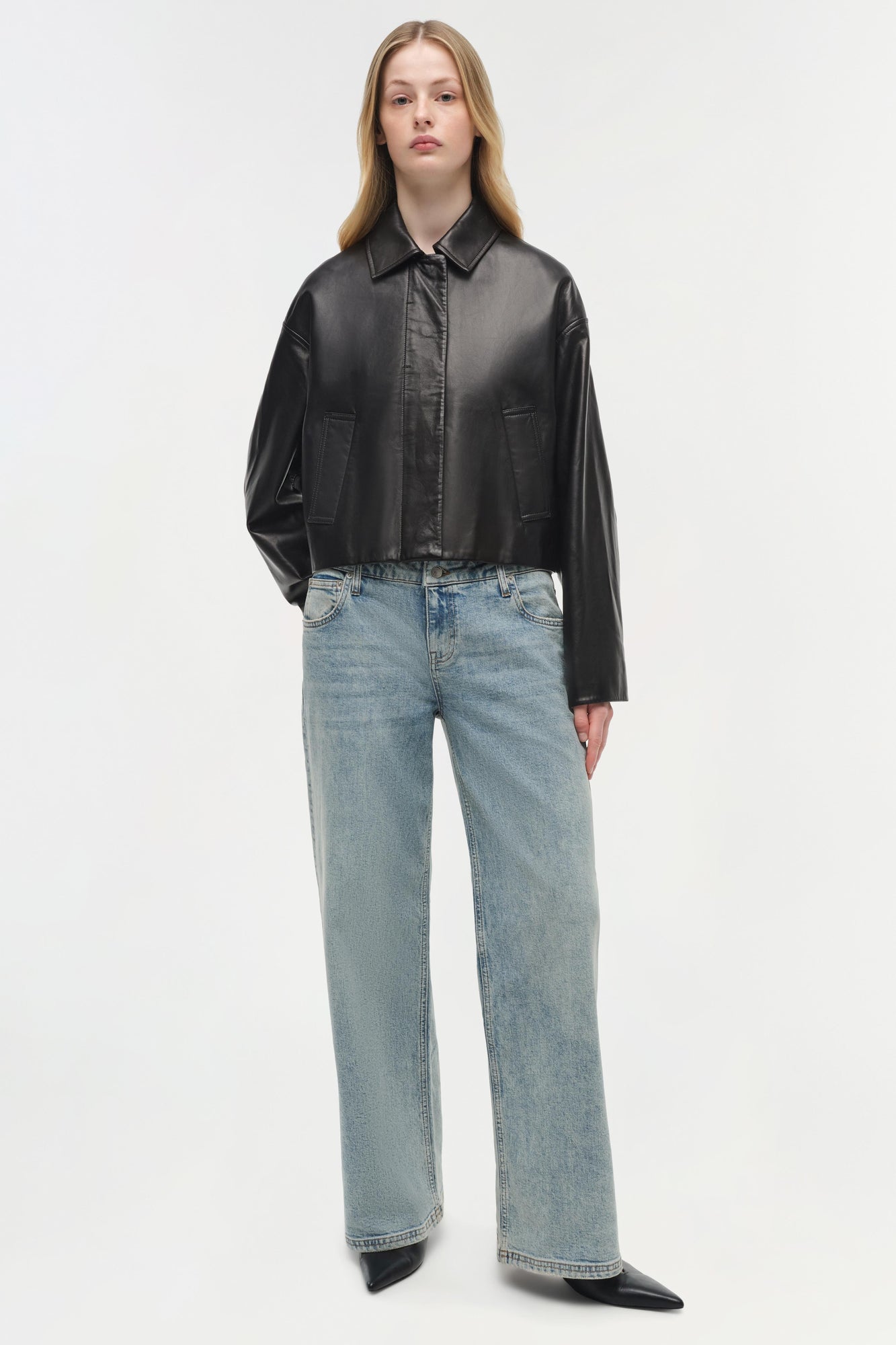 Black leather jacket with pointed collar, button front, and chest pockets worn with light blue jeans.