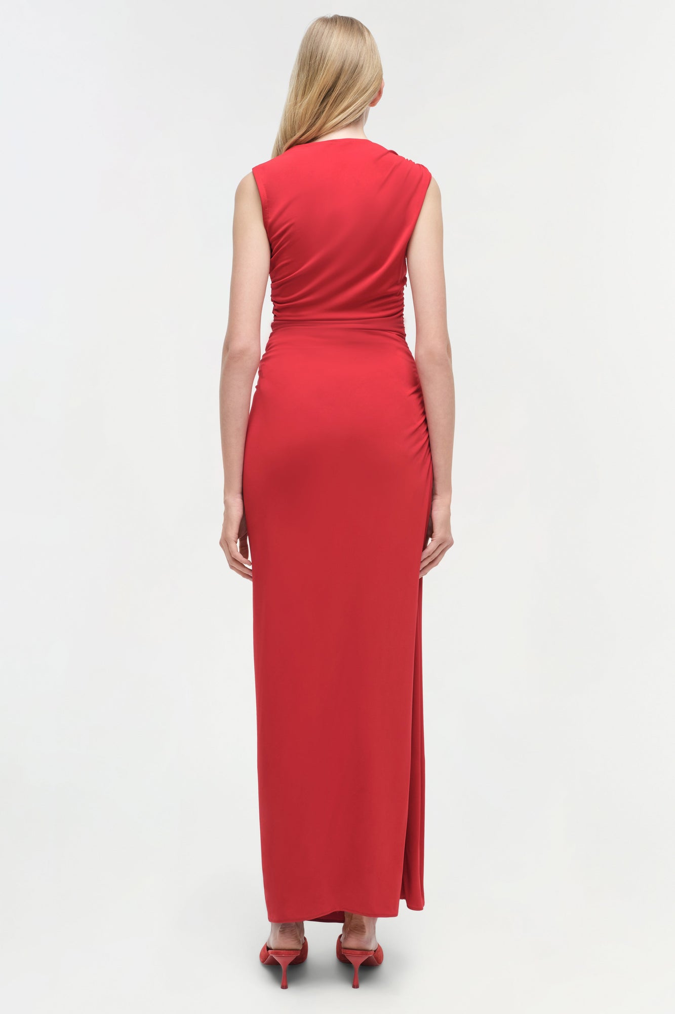 Red sleeveless jersey gown with ruched waist detail and high slit, shown from back view.