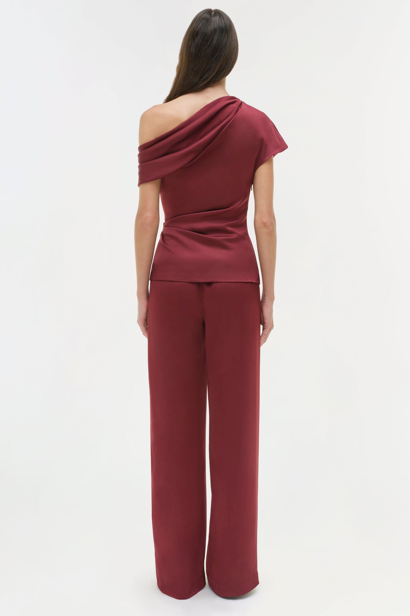 Burgundy draped satin top with one-shoulder neckline and ruched waist detail, shown on model from back.