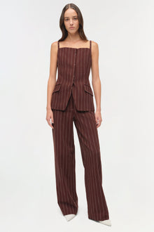 Woman wearing burgundy pinstriped suiting pants with matching sleeveless vest and white pointed-toe shoes.