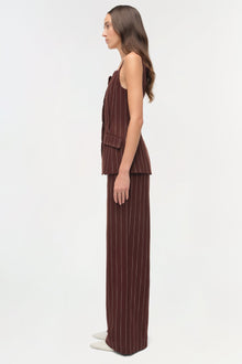 Woman wearing burgundy pinstriped suiting pants with matching sleeveless vest, shown in side profile.