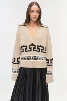 Cream V-neck sweater with black geometric patterns and collared shoulders, paired with black pleated skirt.