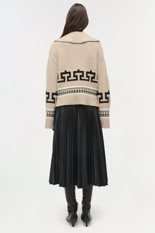 Cream and black geometric patterned V-neck sweater with ribbed collar worn over black pleated skirt.