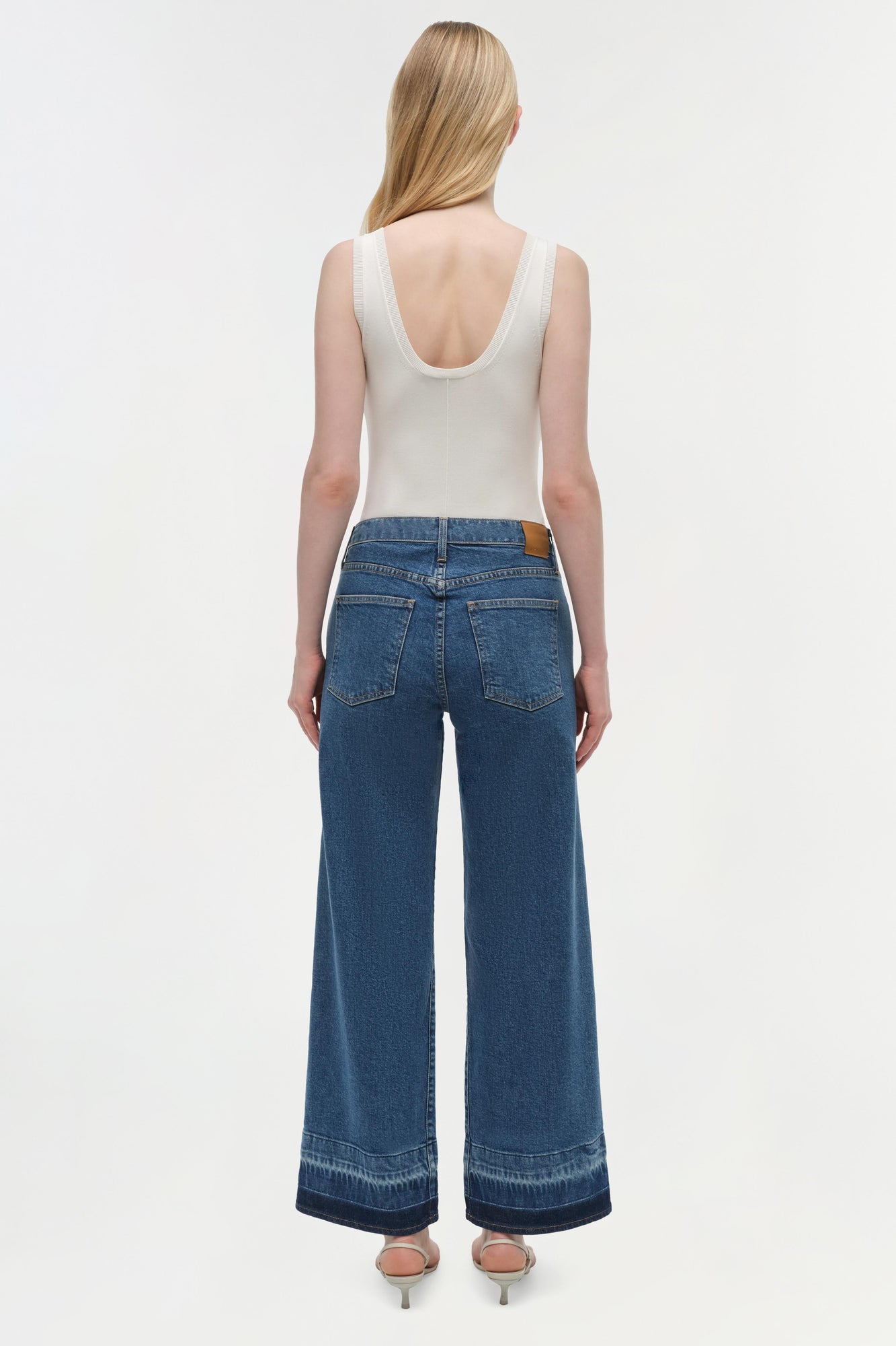 Wide-leg blue denim crop jean with raw hem detail, shown with white sleeveless tank top.