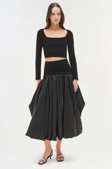Black knit cropped top with long sleeves and square neckline worn with matching waistband and full skirt.