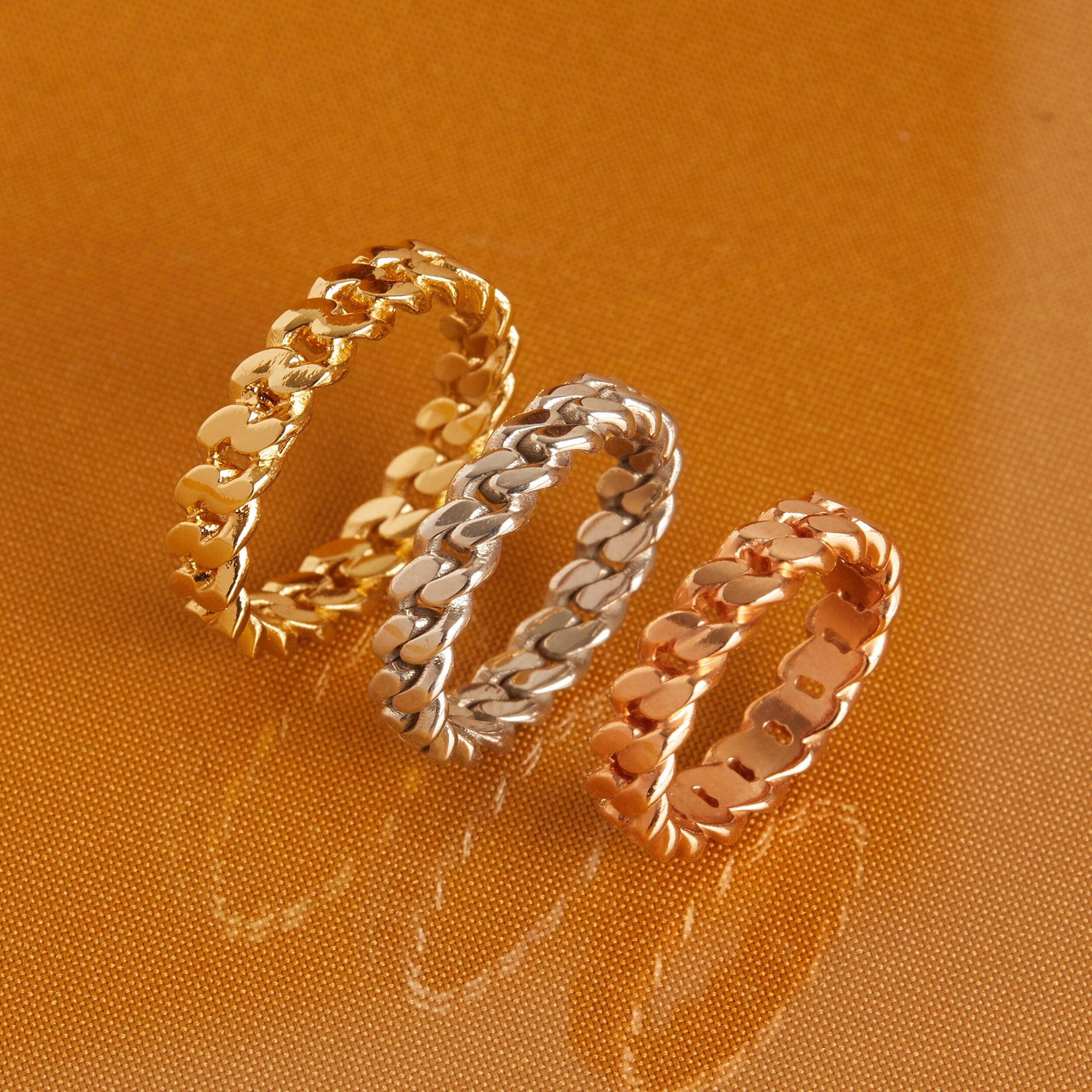 Flatlay Model. Three twisted rings, gold, silver and rose, on orange background
