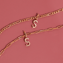 Flatlay Model Close-up of two gold chain necklaces with 'S' pendantsâ€”one solid gold and one diamond-encrustedâ€”resting against a pink background