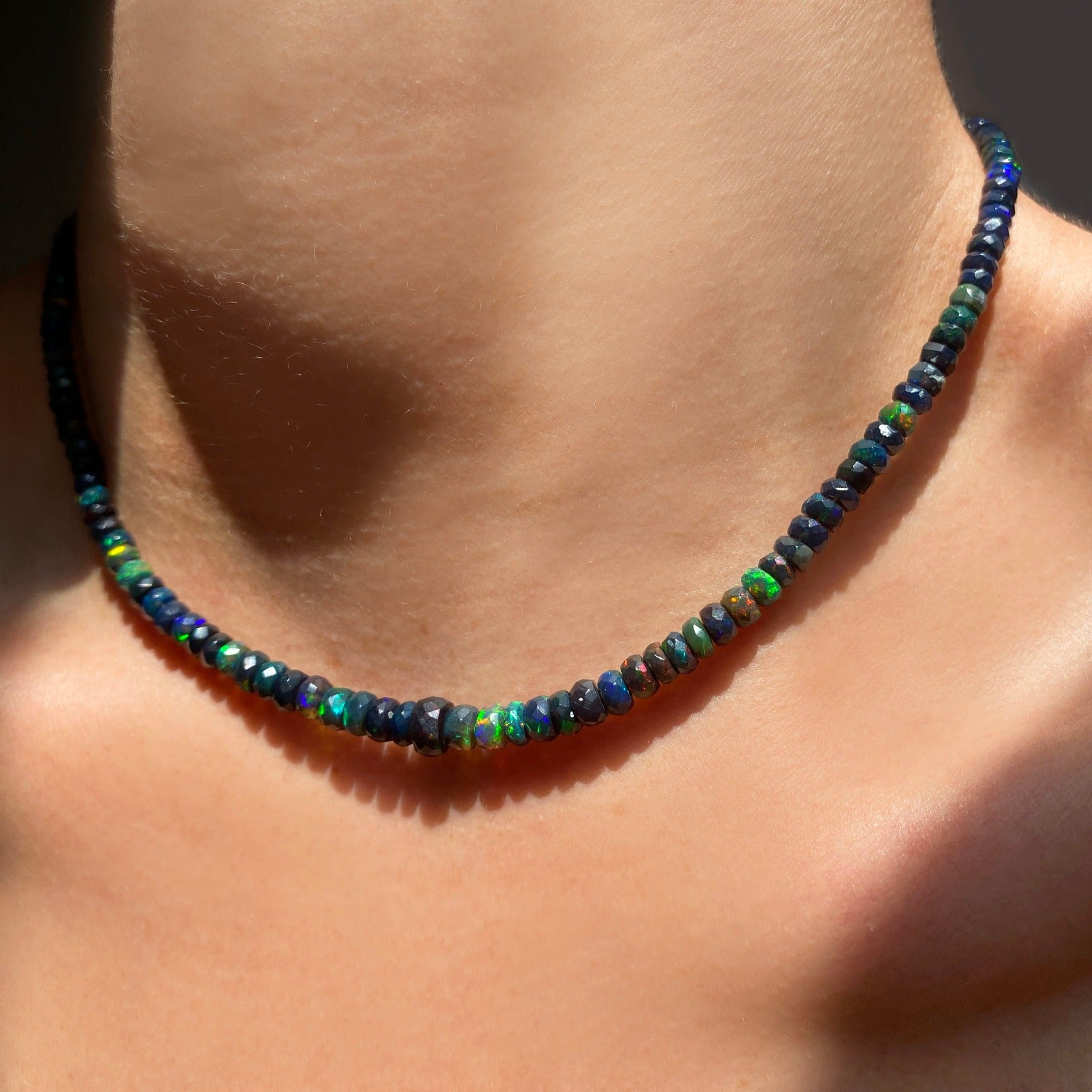 Shimmering beaded necklace made of faceted opals in shades of black, green, and blue on a gold linking ovals clasp. 