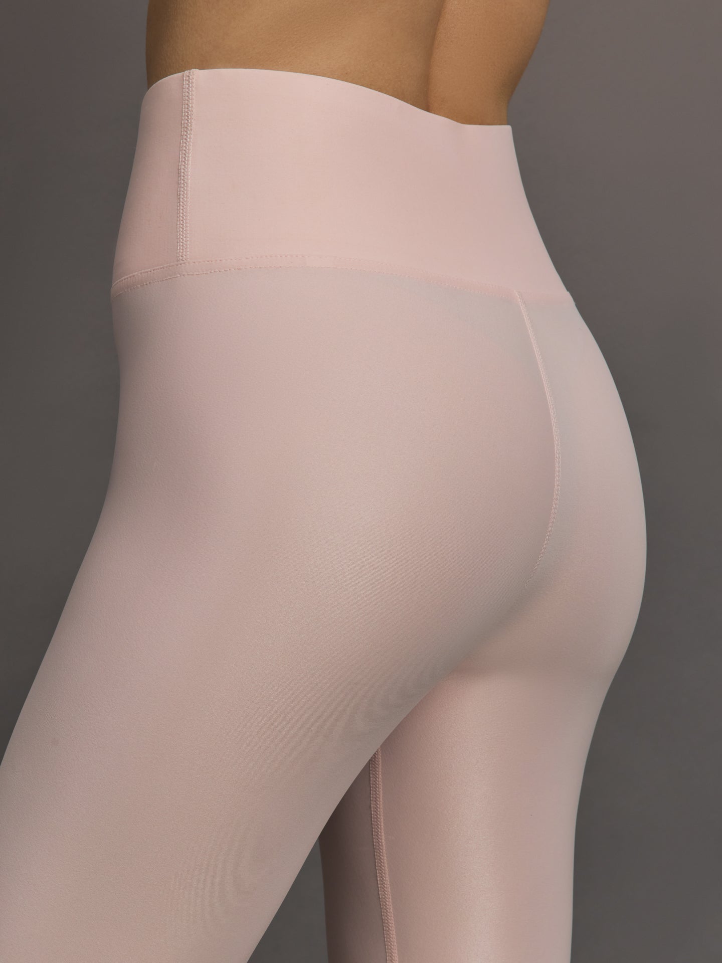 Model wears a pair of high rise baby pink sleek liquidy shine leggings. 