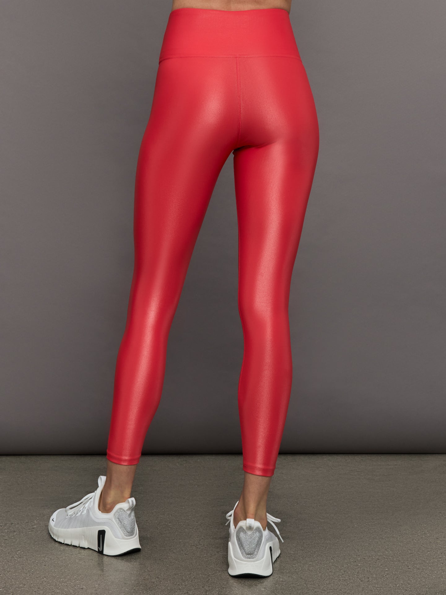 Model wears a high rise pair of bright red leggings with a liquidy shine finish. 