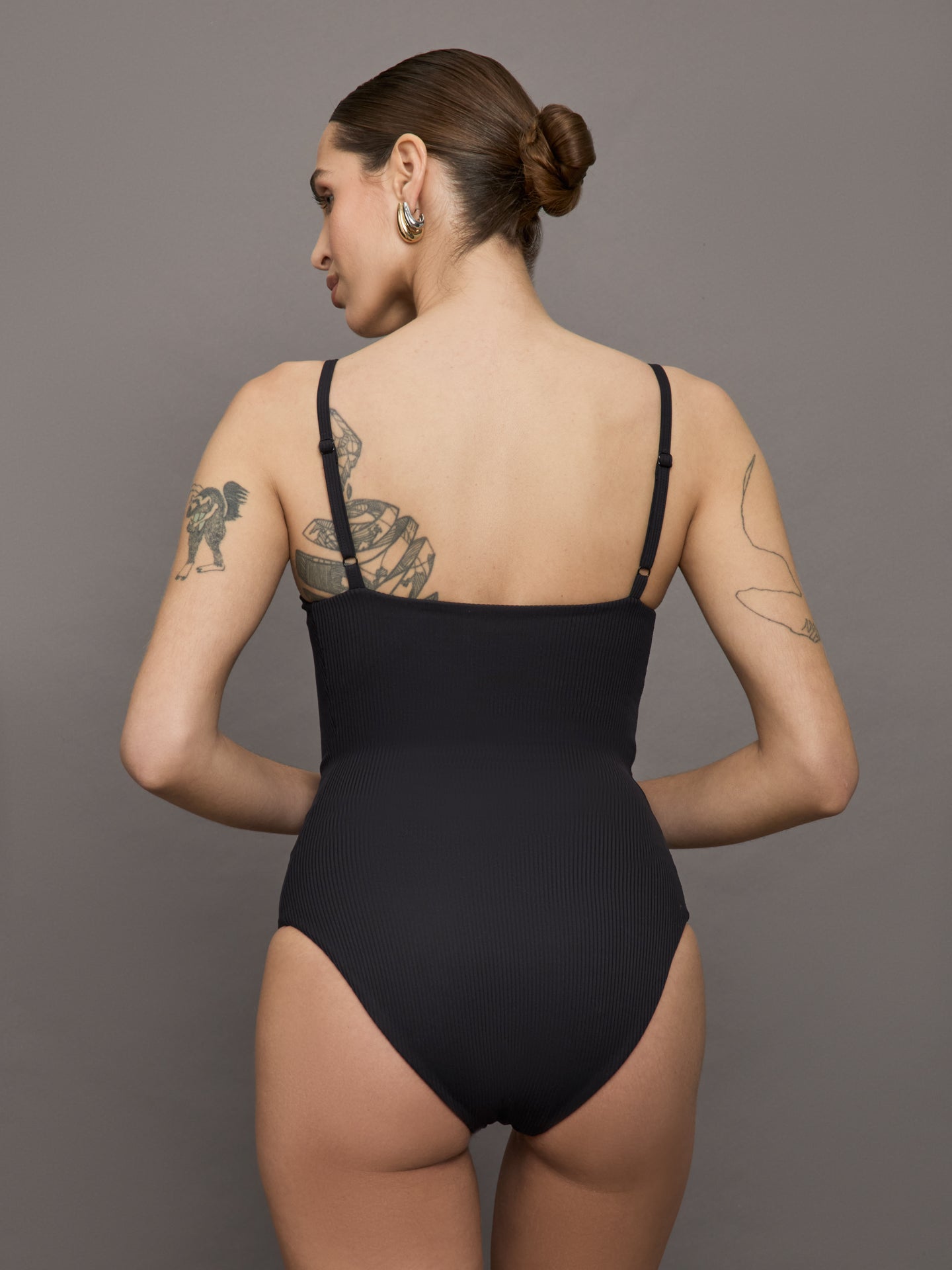 Model wears a black bodysuit with a straight neckline across the chest and thin straps. 