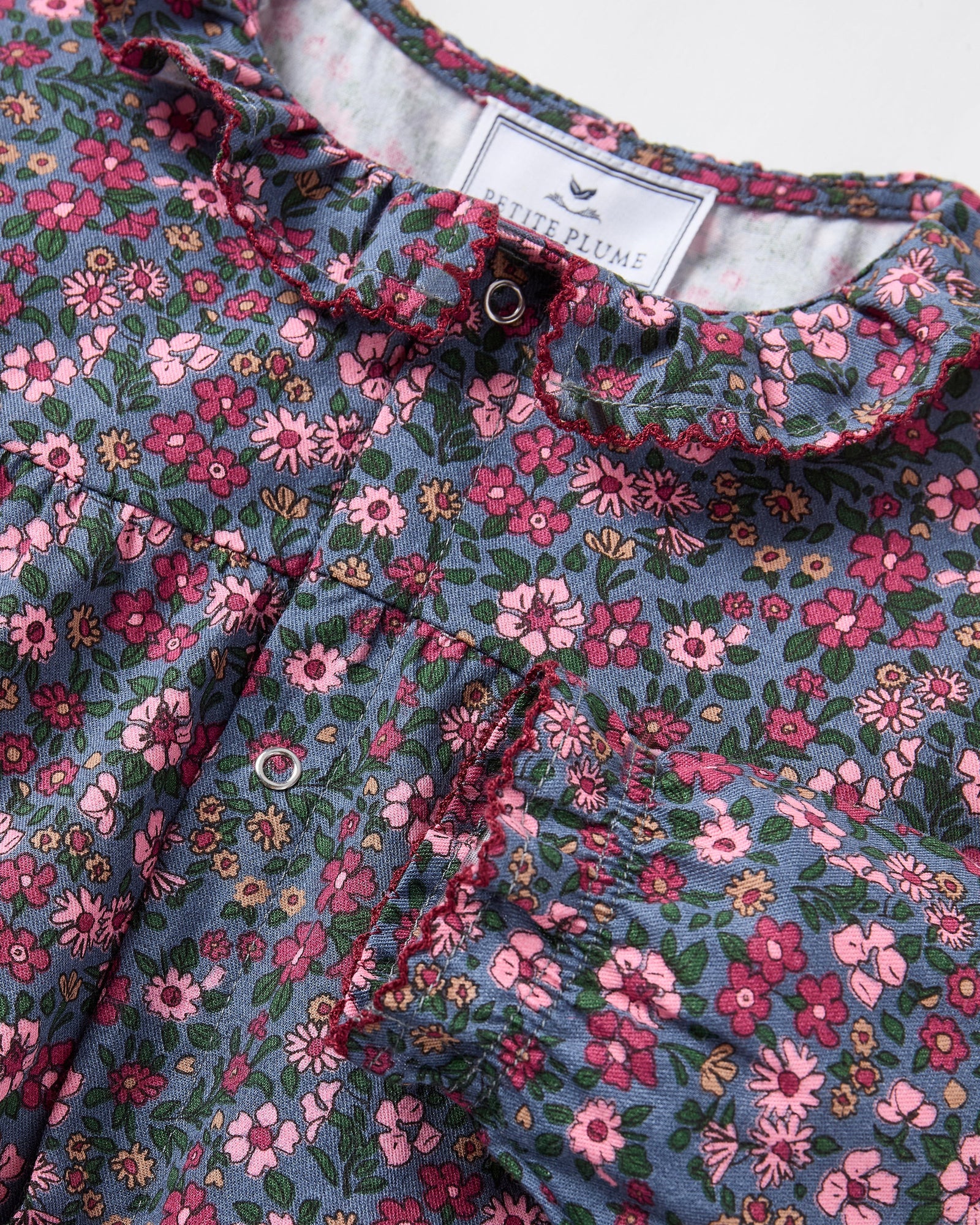 Baby's Twill Madeline Romper in Fleurs de Saison features long sleeves, a dark base with pink and purple floral print, front snap closures, a rounded collar, and gathered cuffs at wrists and ankles.