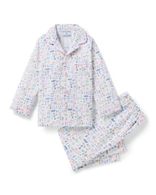 The Kid's Twill Pajama Set in Baking Spirits Bright features white long-sleeve button-up top and long pants with a colorful print of various small household and travel items.