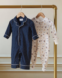 The Baby's Twill Classic Romper in Midnight Hearts is a navy blue onesie with long sleeves and legs, featuring a white heart pattern and white piping on the collar, cuffs, and front.