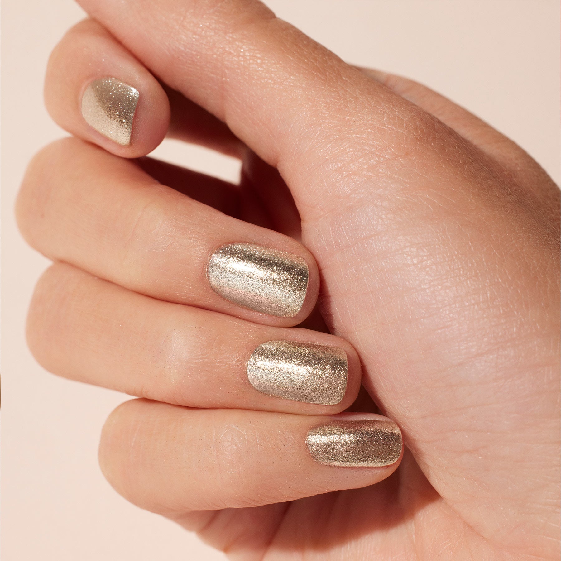 A close-up of a light-skinned hand with neatly manicured nails painted in Manucurist's Glitters Duo Silver  Mirror polish, featuring a shiny metallic finish against a soft neutral background.