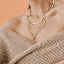 Lifestyle Model Close-up of a woman wearing a beige off-the-shoulder sweater and layered gold necklaces, including one with a diamond-encrusted 'S' pendant.