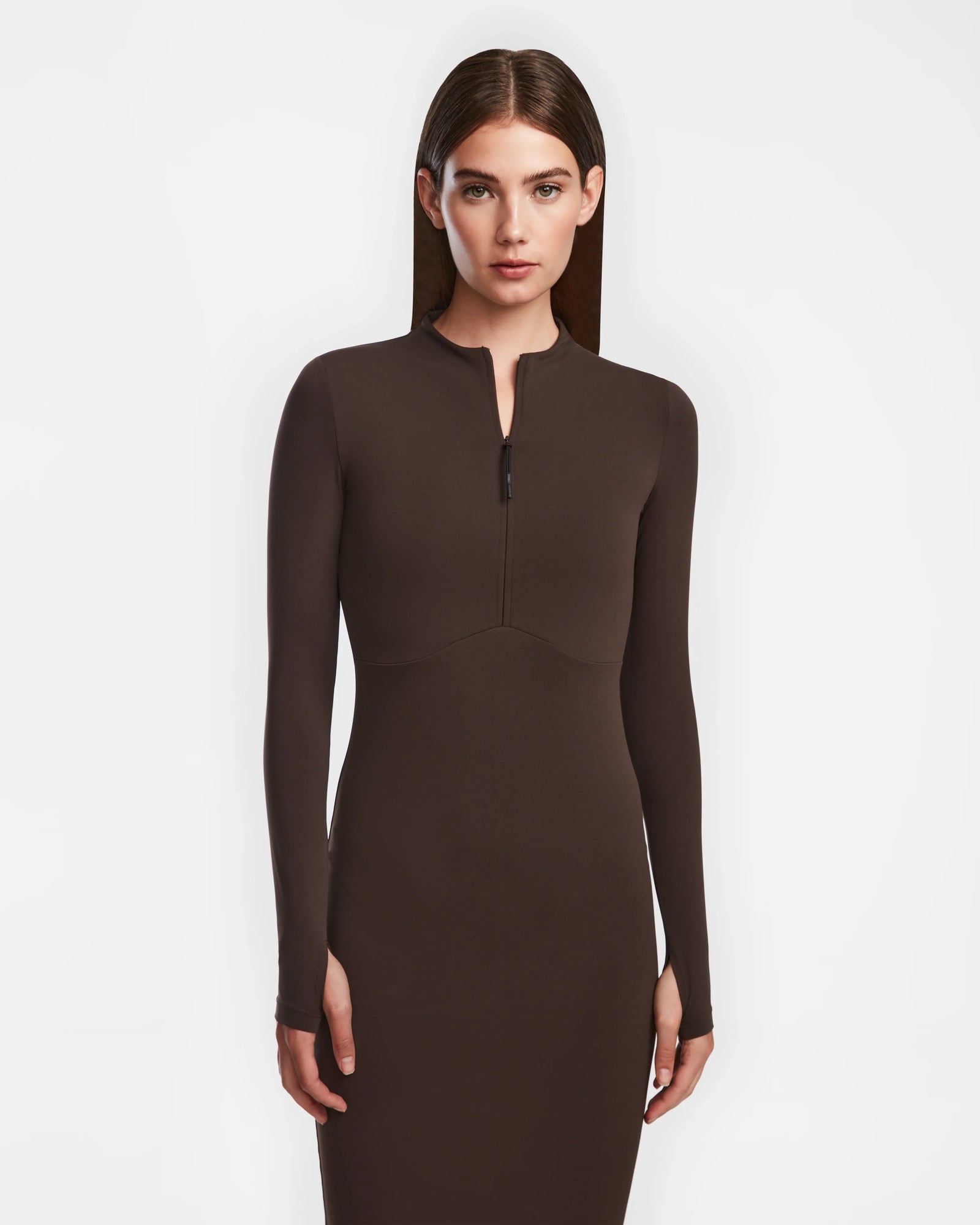 A woman with straight brown hair models the Rudsak AGNES - 8524551 Espresso fitted, long-sleeve zip-up dress against a plain white background, looking directly at the camera.