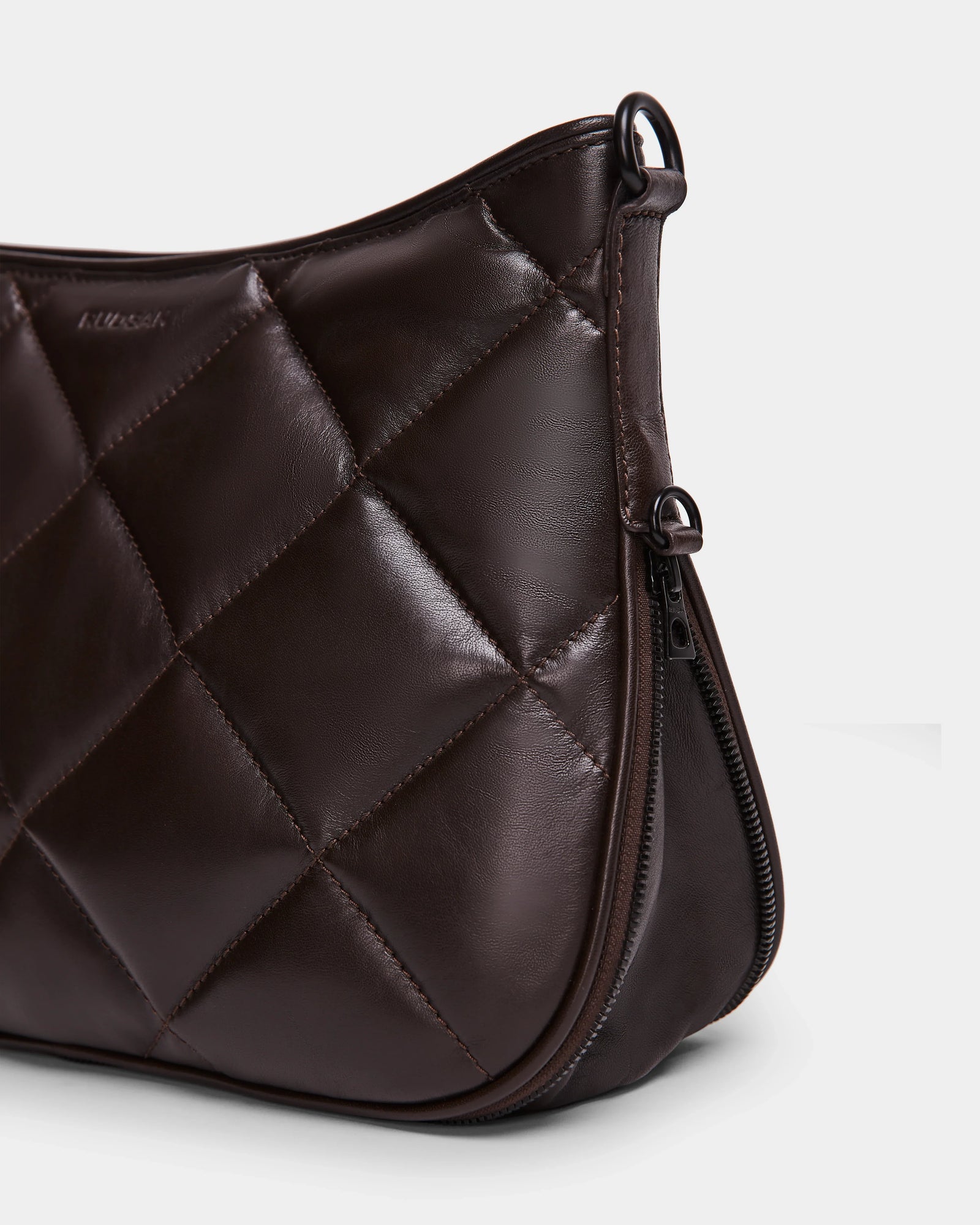 A close-up of the Rudsak ALICIA - 8323507 Espresso womens handbag, featuring luxe leather with diamond quilting, a visible zipper, and a smooth finish, set against a plain light background.