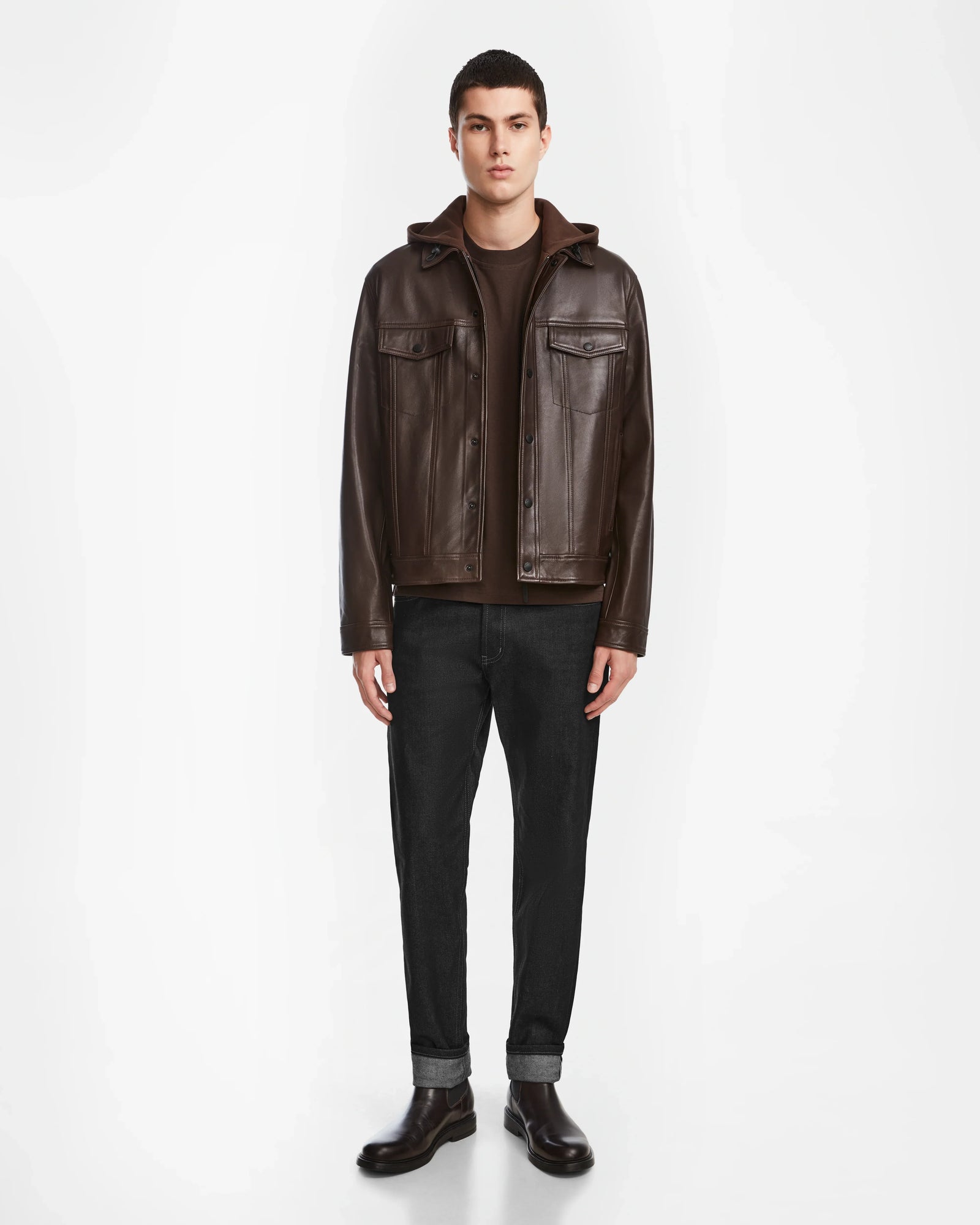 A man faces forward wearing the Rudsak AREN - 6124580 Espresso mens leather shirt jacket over a brown shirt, black cuffed pants, and brown shoes against a plain white background.