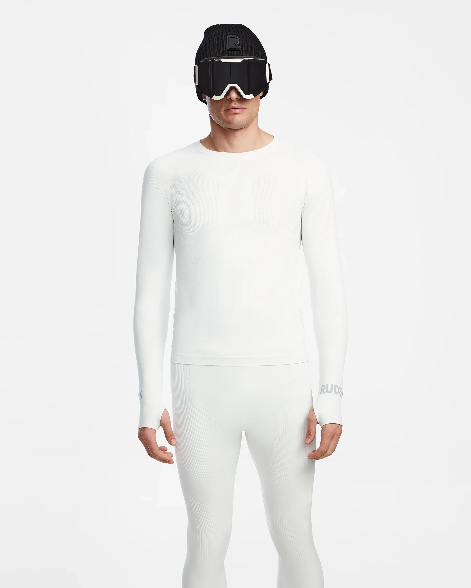 A person wears the fitted, all-white Rudsak FRANC - 6524541 Iceland men’s thermal underwear with white ski goggles and a black beanie, standing against a white background. This sleek set is the ideal skiing underlayer for a modern look.