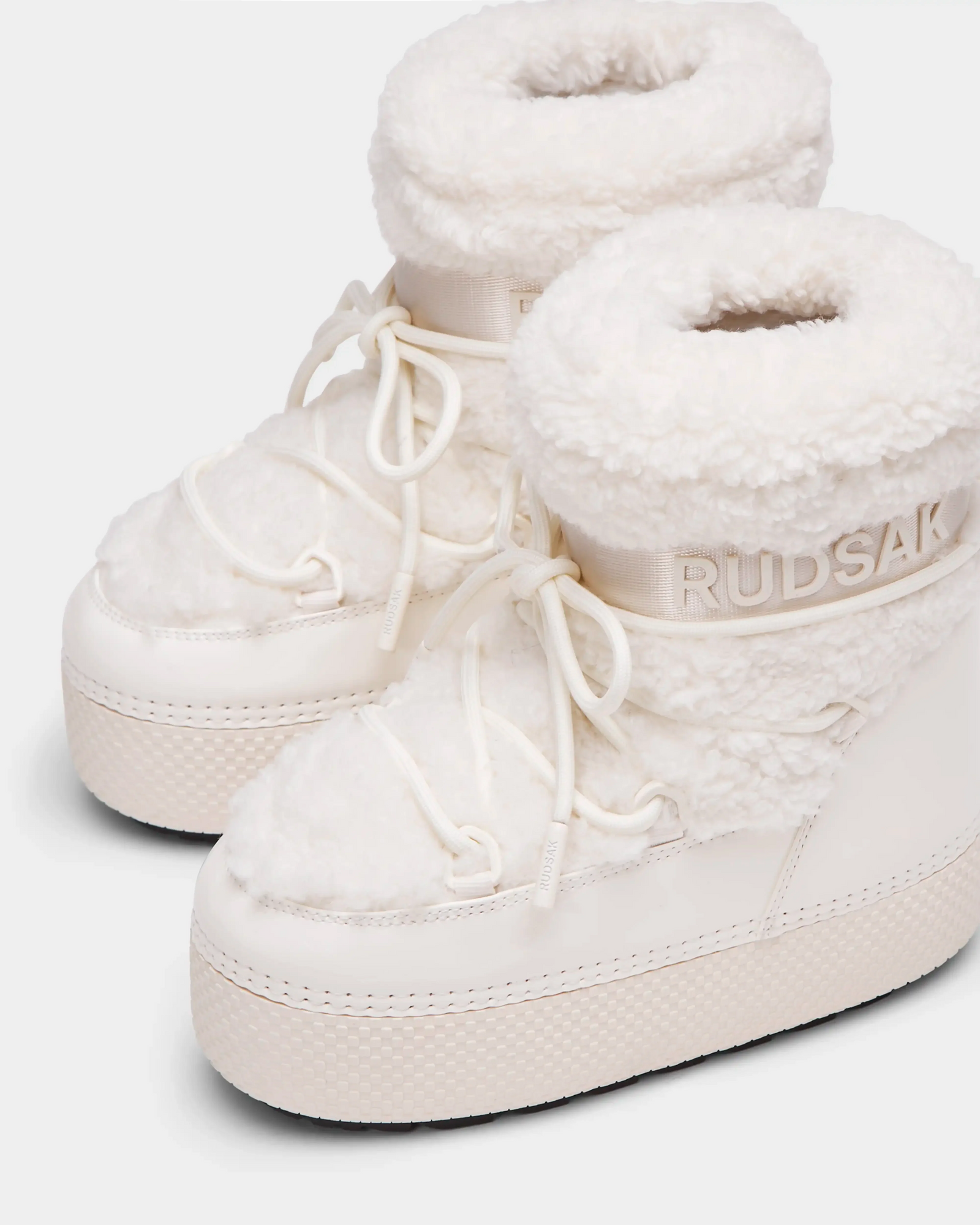 The KATHY Y - 1224500 Iceland by Rudsak are white winter boots featuring thick soles, plush faux fur trim and lining, lace-up fronts, water-repellent finish, and Rudsak branding embossed on the side.