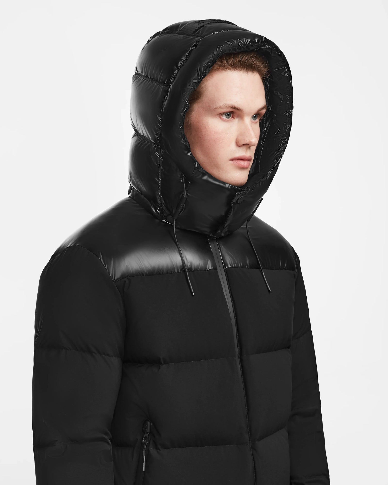 A young person wears the Rudsak THEO - M125531 Black weather-resistant puffer jacket with a shiny hood up, looking to the side against a plain white background.