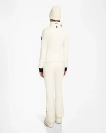A person faces away in an all-white Rudsak ROSALIE - 8124784 Iceland winter look, featuring a women’s fitted ski jacket with RECCO rescue tech, flared pants, and beanie, set against a plain white background.