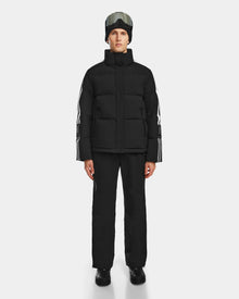 A person wearing the Rudsak USHER - 6124516 Black water-resistant ski jacket and pants, black boots, a black beanie, and ski goggles stands facing forward against a plain white background.