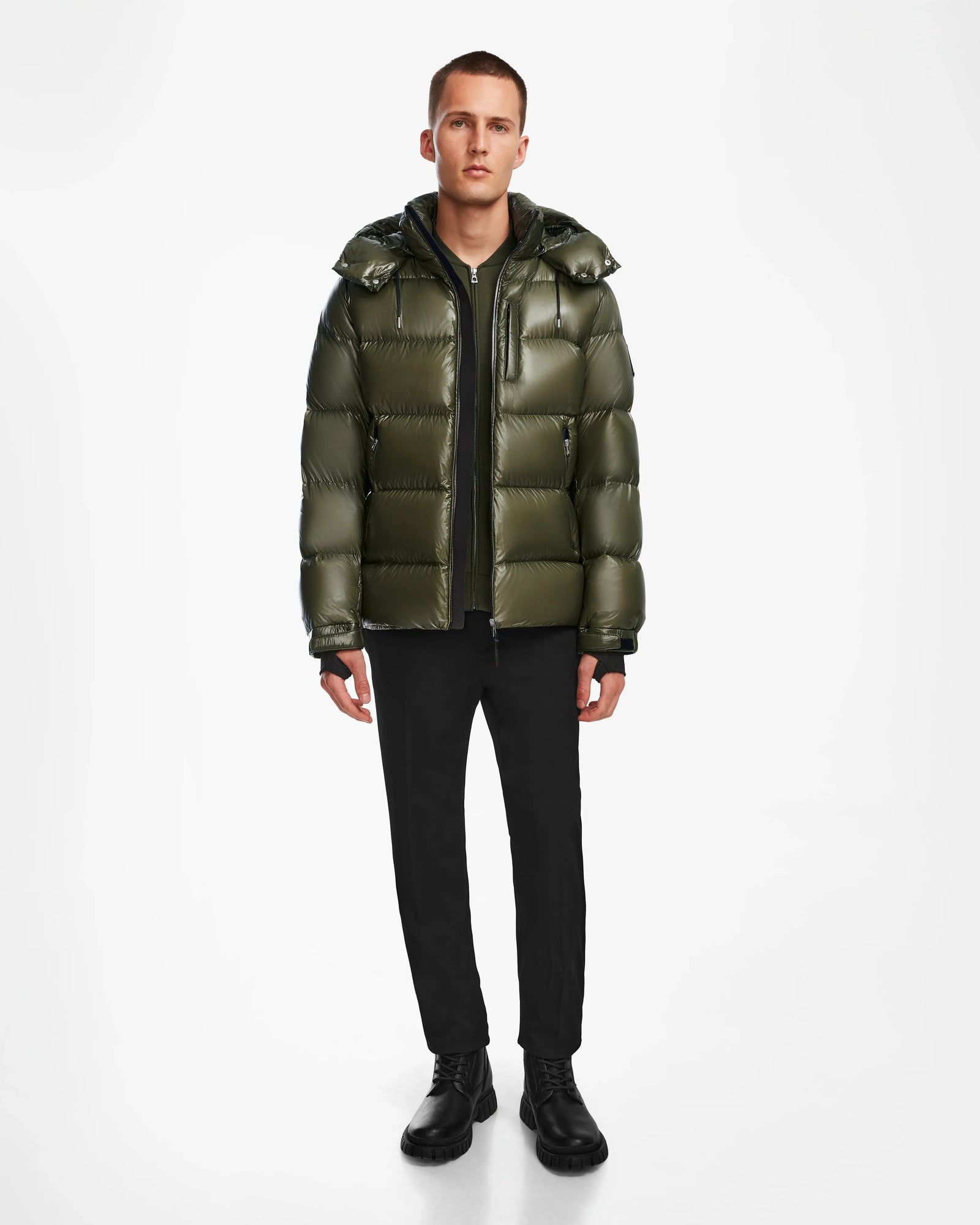 A man faces forward wearing the Rudsak VINCE S - 6124560 Loden Green men’s down puffer jacket, styled with black pants, shirt, and boots—ideal for cold-weather layering—set against a plain white background.