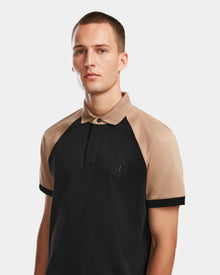 A man with short hair wears the Rudsak WALTER - 6524531 polo in black/camel—premium cotton, tan sleeves, black body—standing against a plain light background.