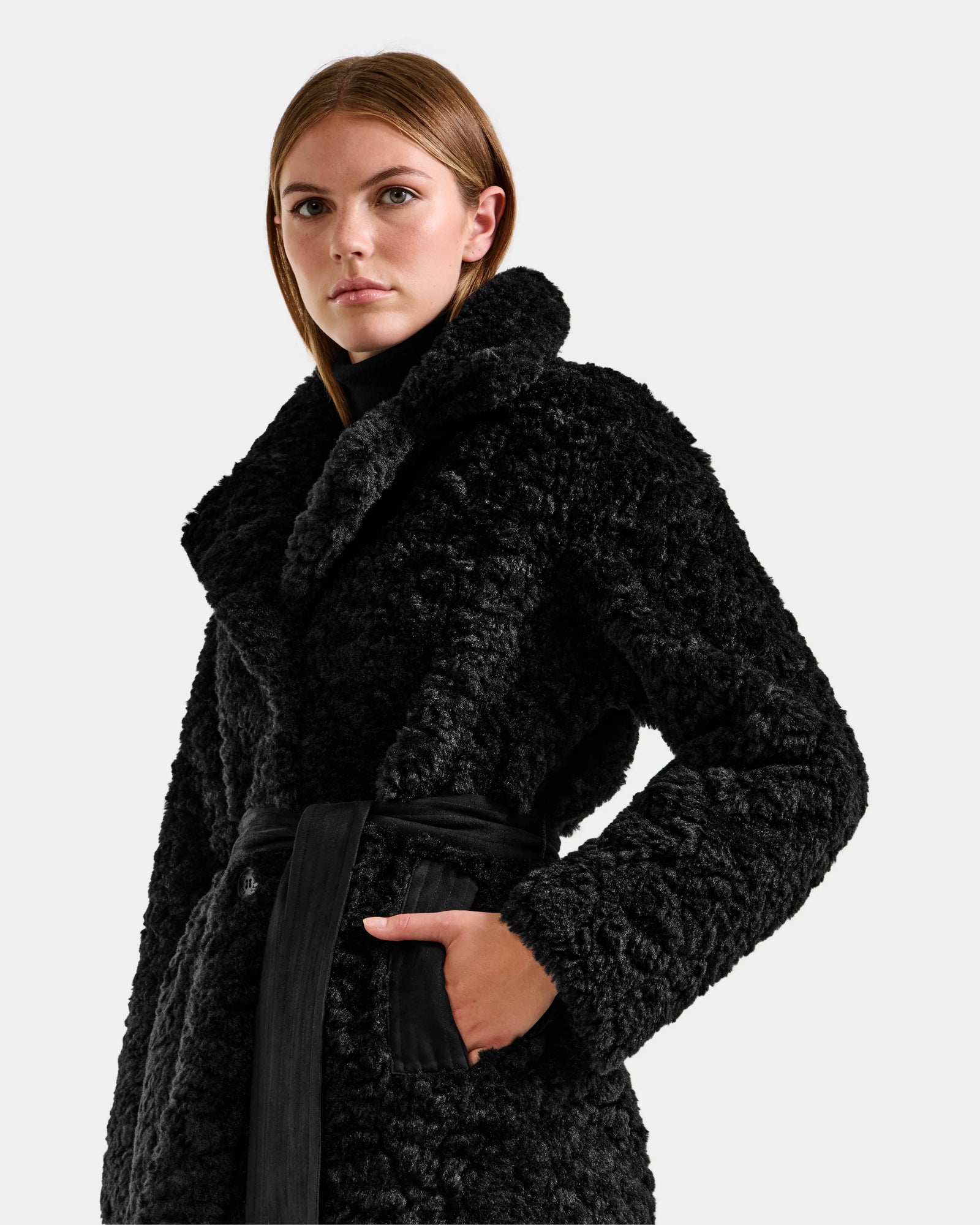 A woman confidently poses against a plain light background wearing the Rudsak ANNABELLE FSU - L125512 Black sherpa teddy trench coat, featuring a wide collar and black belt.