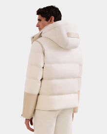 A person is seen from the back, looking to the side against a white background, wearing the Rudsak DAVID - M125508 Vanilla puffy lamb shearling hooded winter jacket with beige sleeves and white pants.