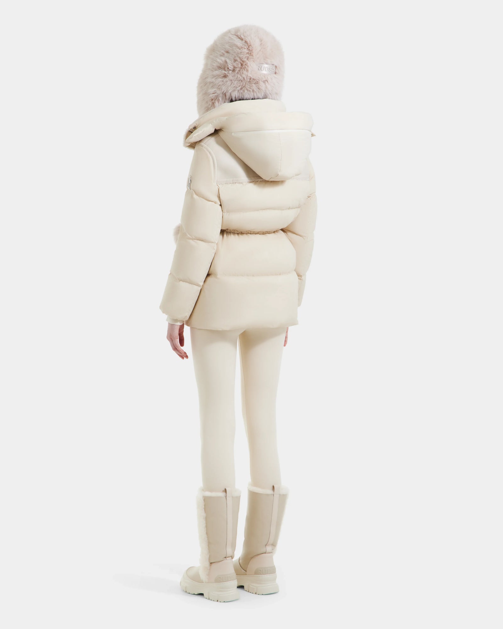 A person stands facing away, wearing the Rudsak EMBER M-M - L125524 Vanilla down puffer with a hood, against a plain white background.