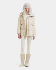 A person faces forward against a white background, wearing the Rudsak EMBER M-M - L125524 Vanilla women's down puffer in cream, matching pants, a furry hat, and tall boots.