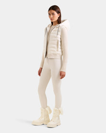 A woman stands in a neutral pose wearing the Rudsak EMILY - L125515 Vanilla off-white hooded down bomber jacket with matching fitted leggings and white lace-up winter boots, against a plain light background.