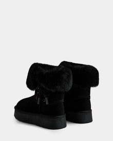 The Rudsak INESA - L225026 Black women's suede platform boots feature thick faux fur cuffs, flat soles, cozy wool lining, and decorative side bows. Shown on a white background.