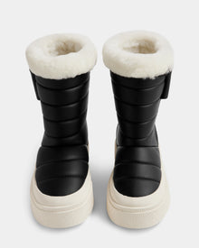 The Rudsak KATHIE - L225516 Black vegan leather winter boots feature thick white fur lining and chunky white soles, displayed front-facing on a plain light background.