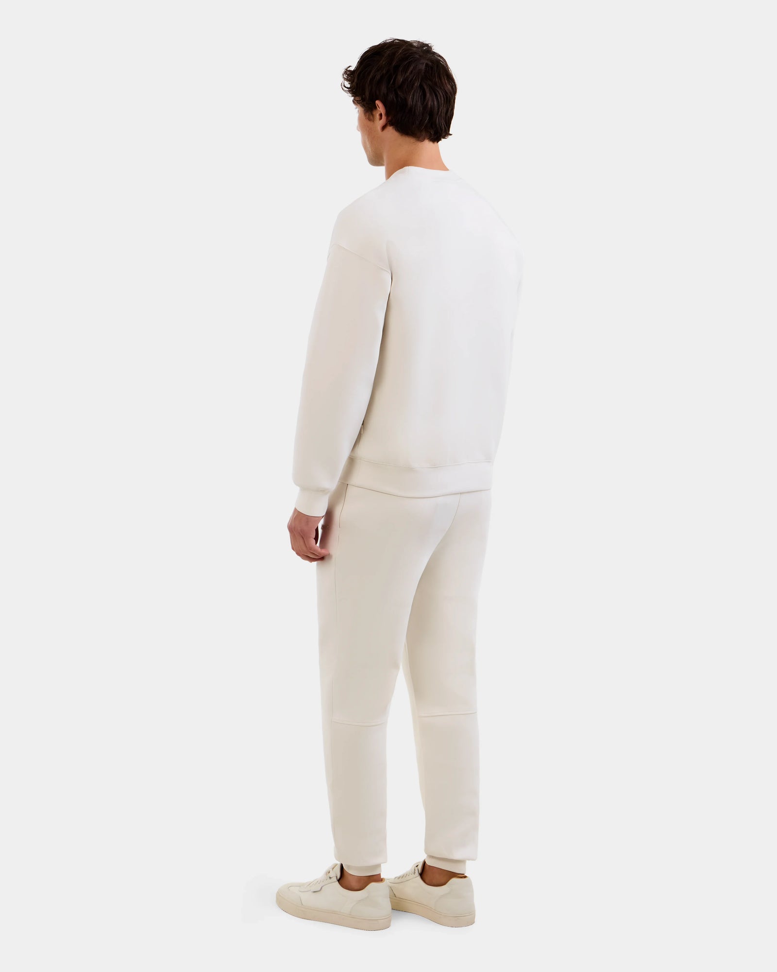 A person faces away from the camera, dressed in Rudsak's MAXTON - U525007 Vanilla M cotton-blend joggers, a matching long-sleeve top, and white sneakers, all set against a plain light background.